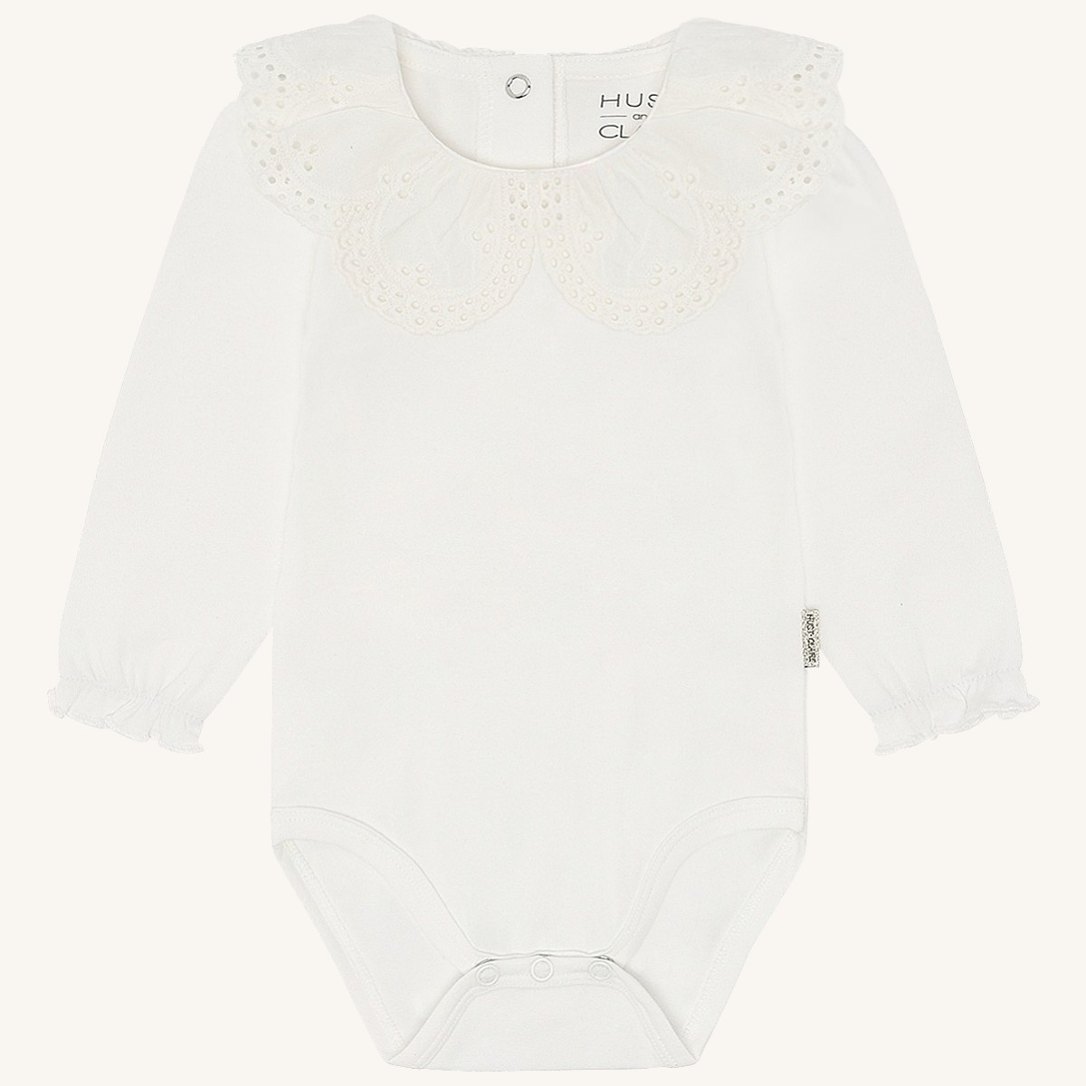 Hvit langermet babybody med brodert krave, rysjemansjetter og trykknapper.