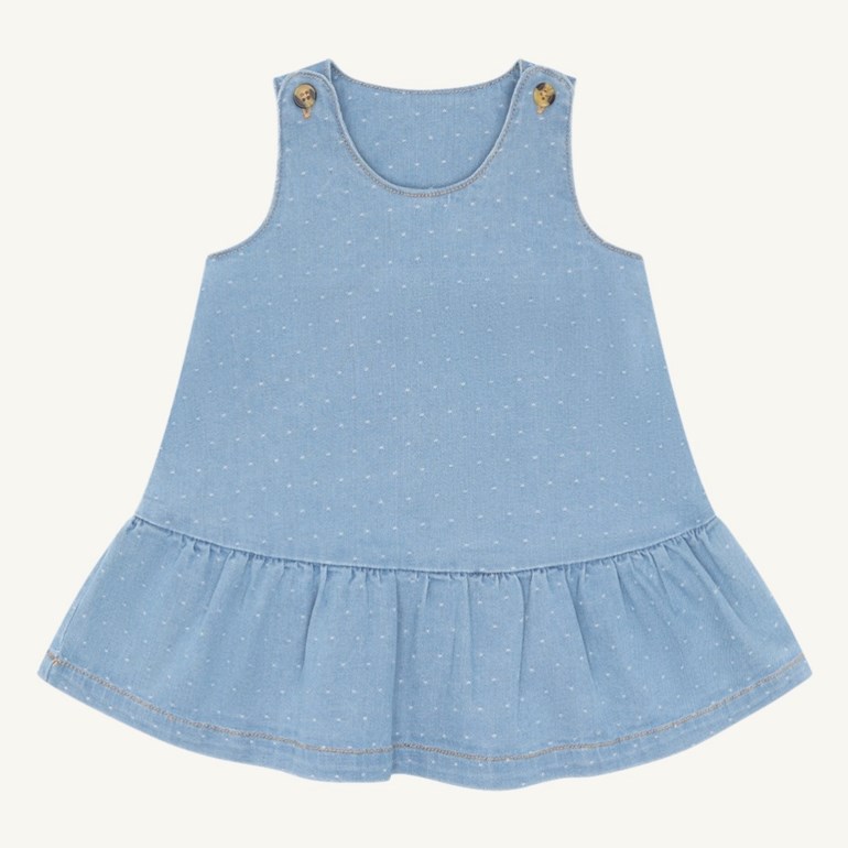 En lyseblå babykjole i denim med hvite prikker, to brune skulderknapper og en volangkant.