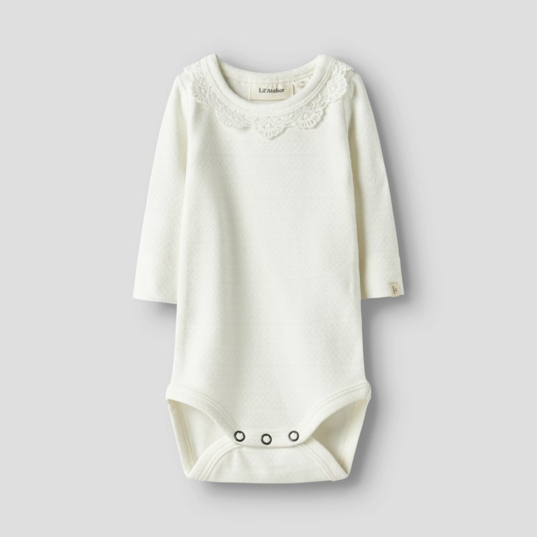 Off-white babybody med lange ermer, blondekantet rund hals, tre trykknapper i skrittet og subtilt teksturert stoff, forfra.