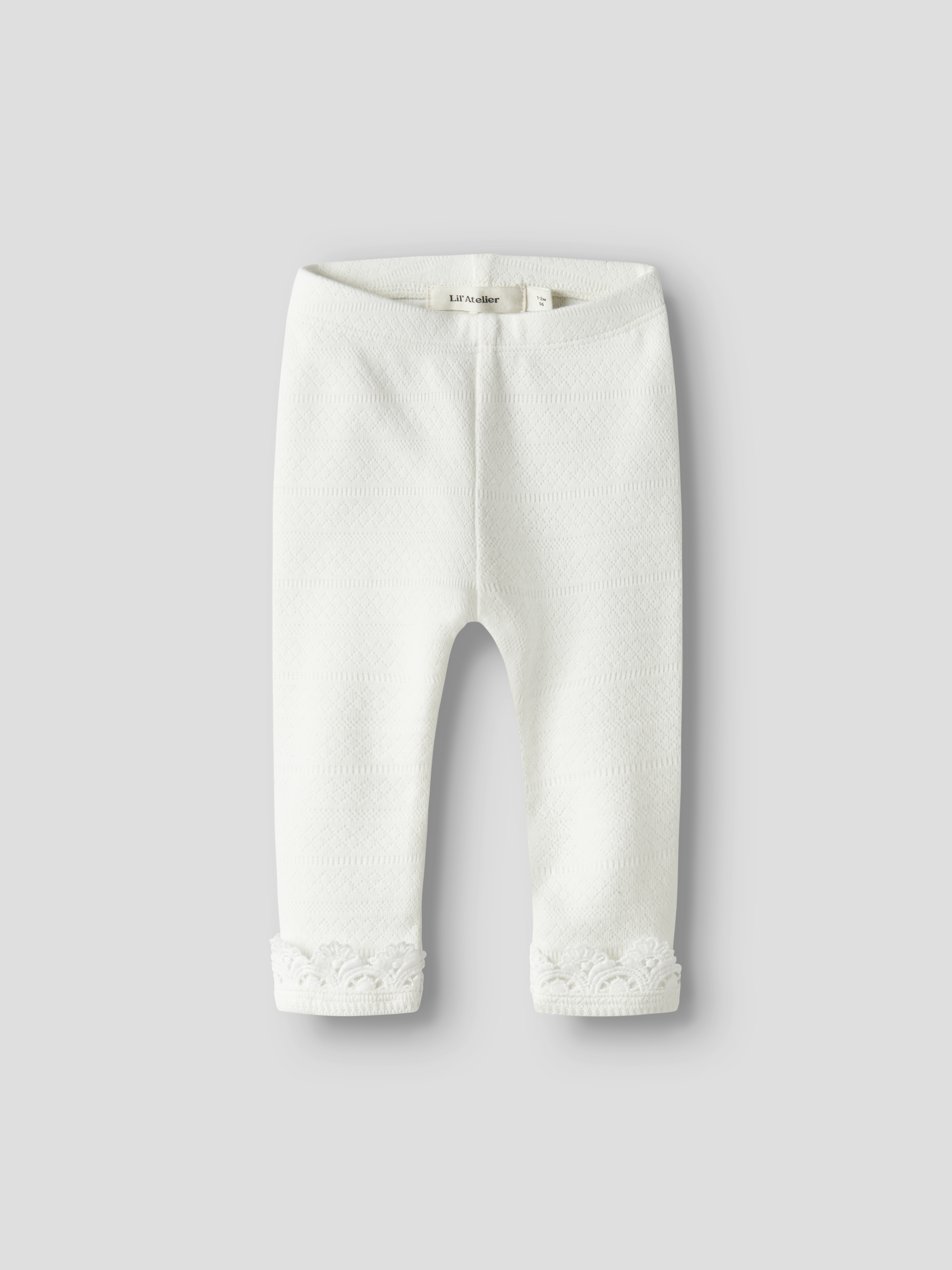 Hvite teksturerte strikkede baby leggings med subtilt diamantmønster og blondemansjetter, forfra.