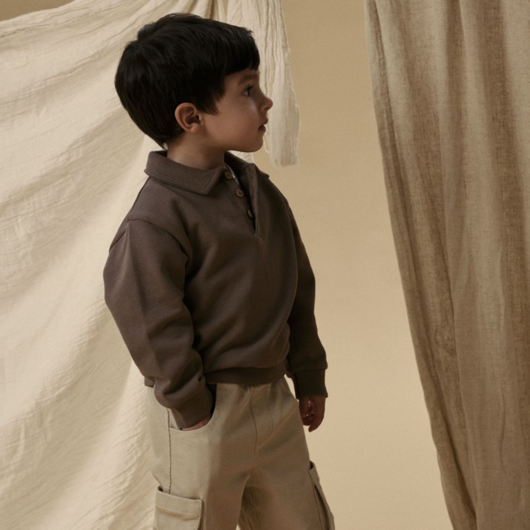 Barn i brun langermet poloskjorte med knappelukking, beige cargobukse og brune sko, sidevisning.
