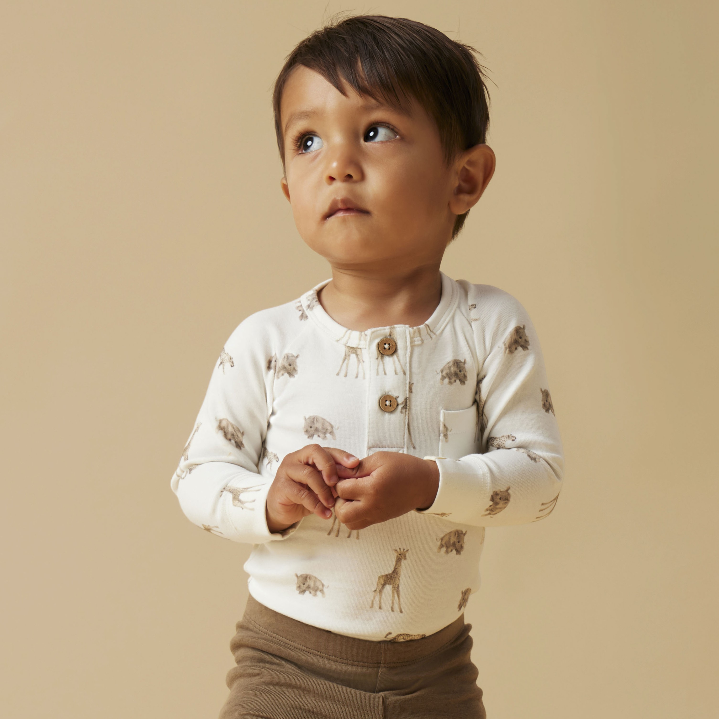 Baby har på seg en kremfarget langermet topp med dyremønster, brune leggings og brune snørestøvler.