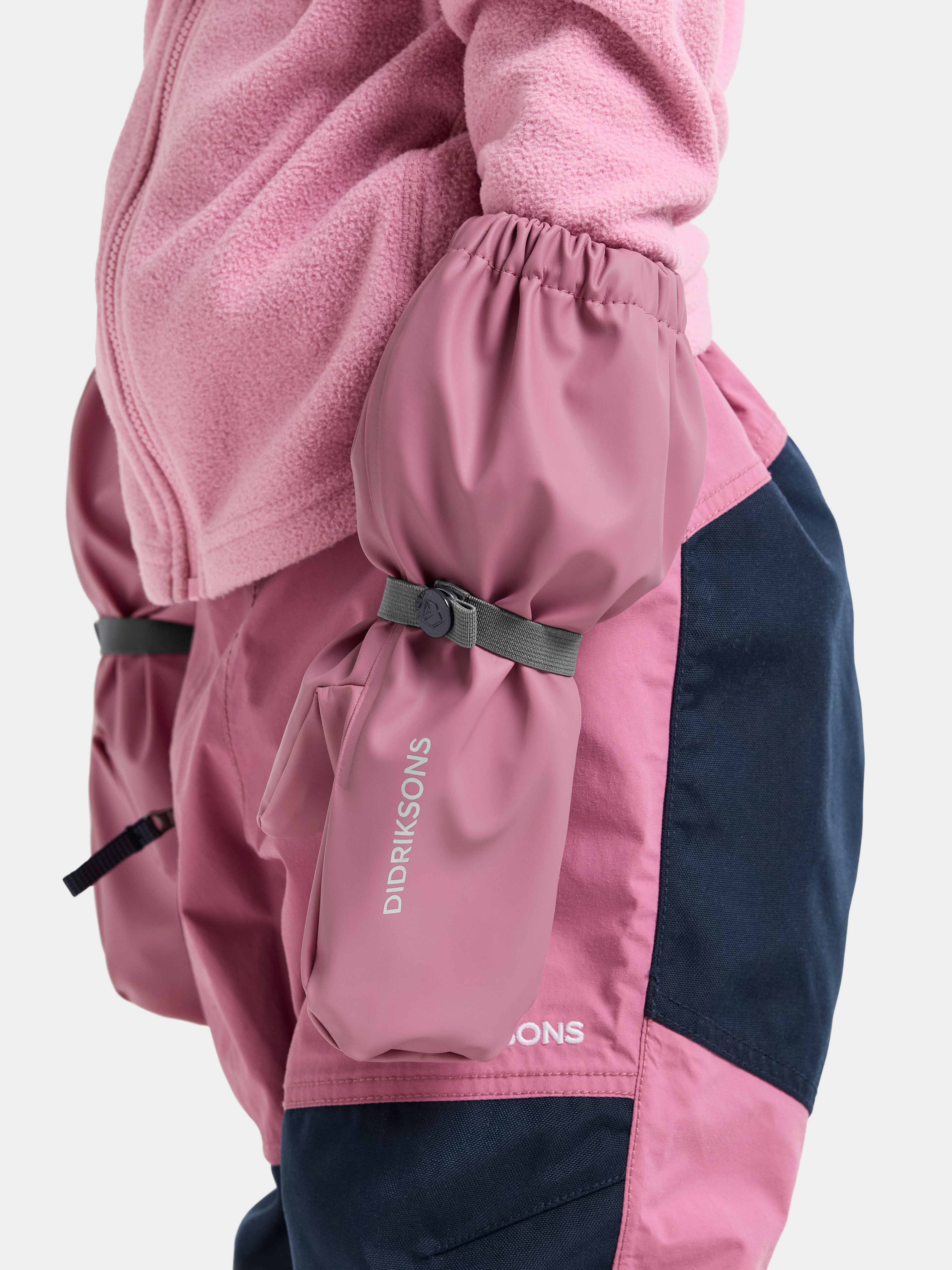 Nærbilde, sidevisning av barn i rosa fleece og støvrosa, mørkeblå vanntett overall med påsydde votter.