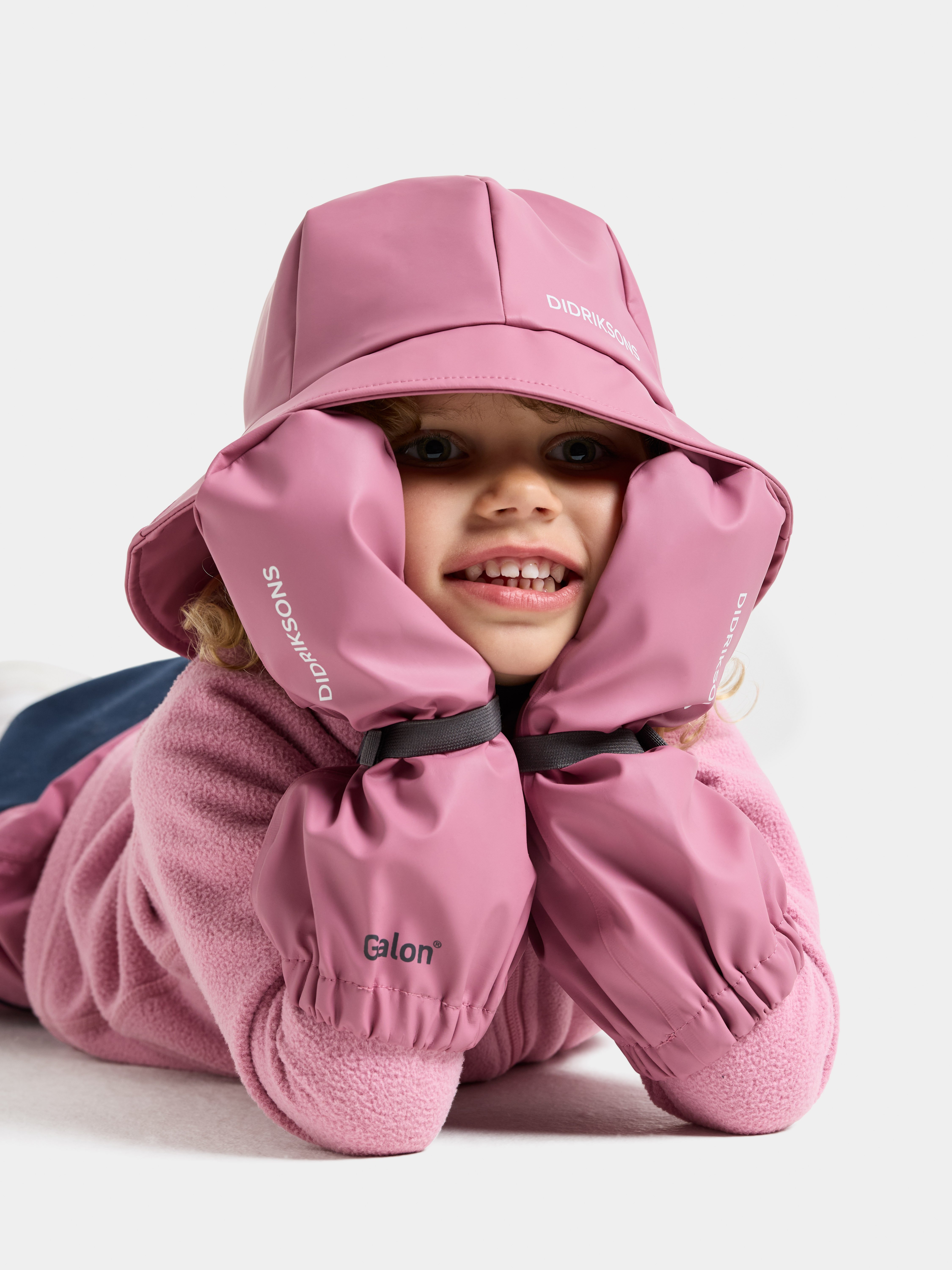 Barn har på seg en pudderrosa regnhatt, matchende Galon® regnvotter og en pudderrosa fleecejakke.
