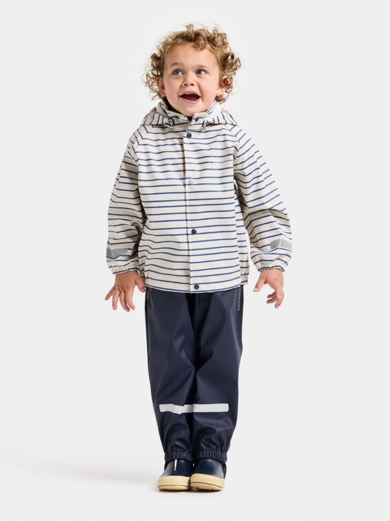 Barn i stripet beige og marineblå regnjakke med hette, marineblå regnbukser og marineblå gummistøvler.