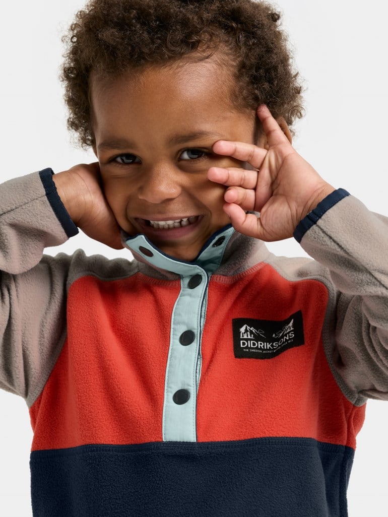 Barns fargeblokket fleecegenser i beige, oransje og mørkeblått med lyseblå knappestolpe.