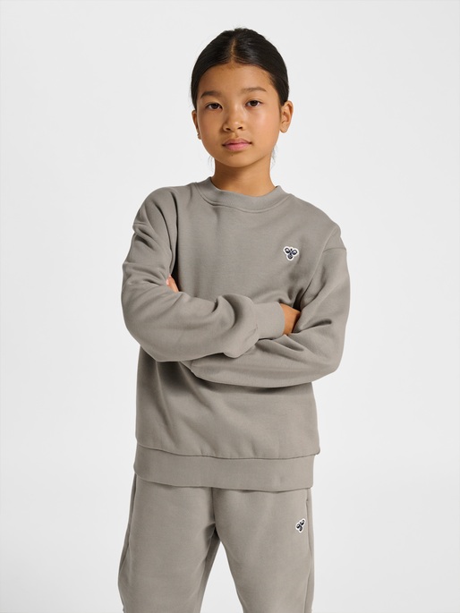 Barn iført grå langermet genser med brystlogo og matchende grå joggebukse med lårlogo.