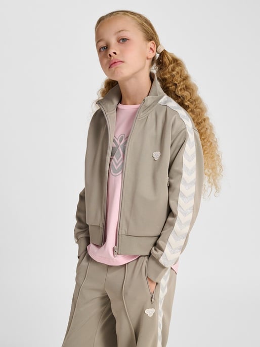 Barn har på seg beig treningsjakke med glidelås, siksakstriper, over rosa t-skjorte og matchende bukser.