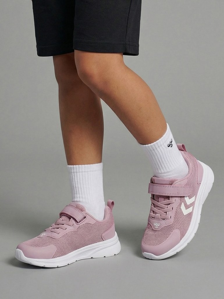 Barn bærer rosa netting joggesko med borrelås og hvite såler, hvite sokker og svarte shorts.