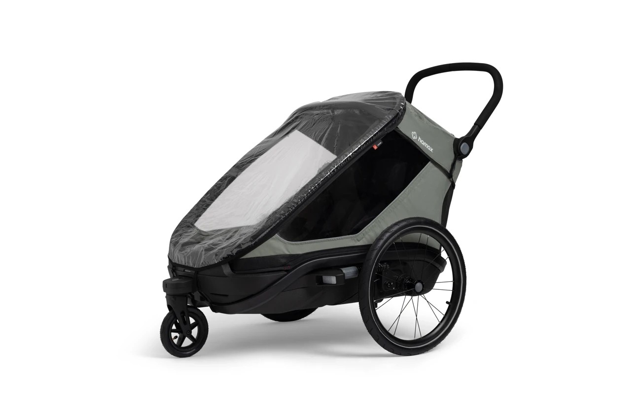 En grå og svart Hamax sykkelvogn for barn med klart regntrekk og hjul, sett fra siden.