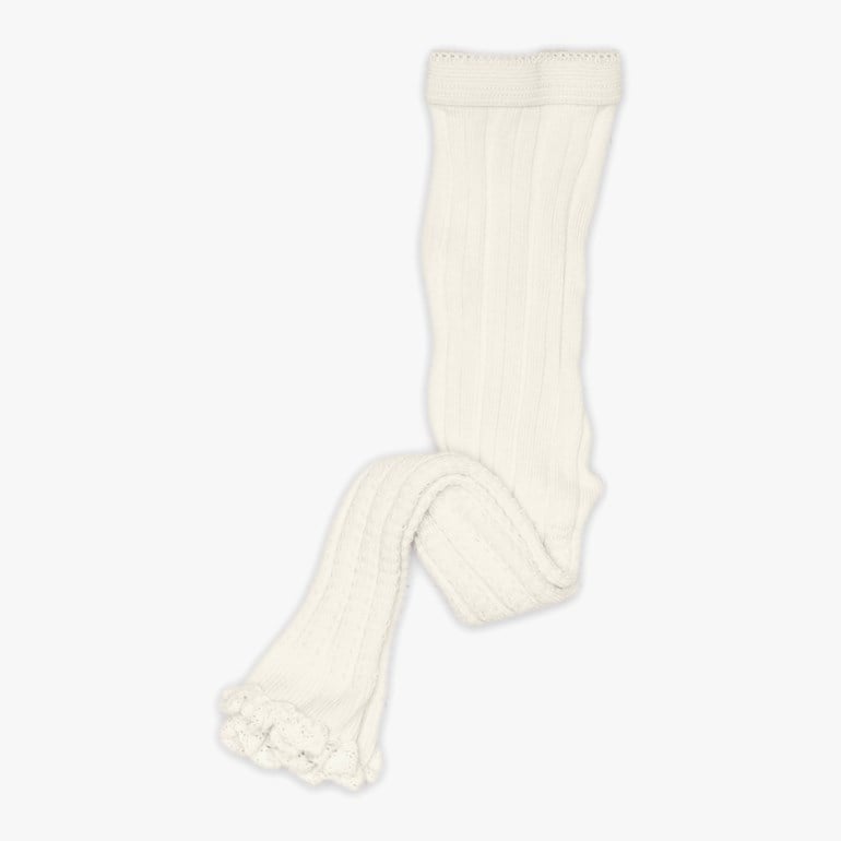 Kremhvite ribbestrikkede babystrømpebukser med dekorativ volangkant ved anklene, lagt flatt.