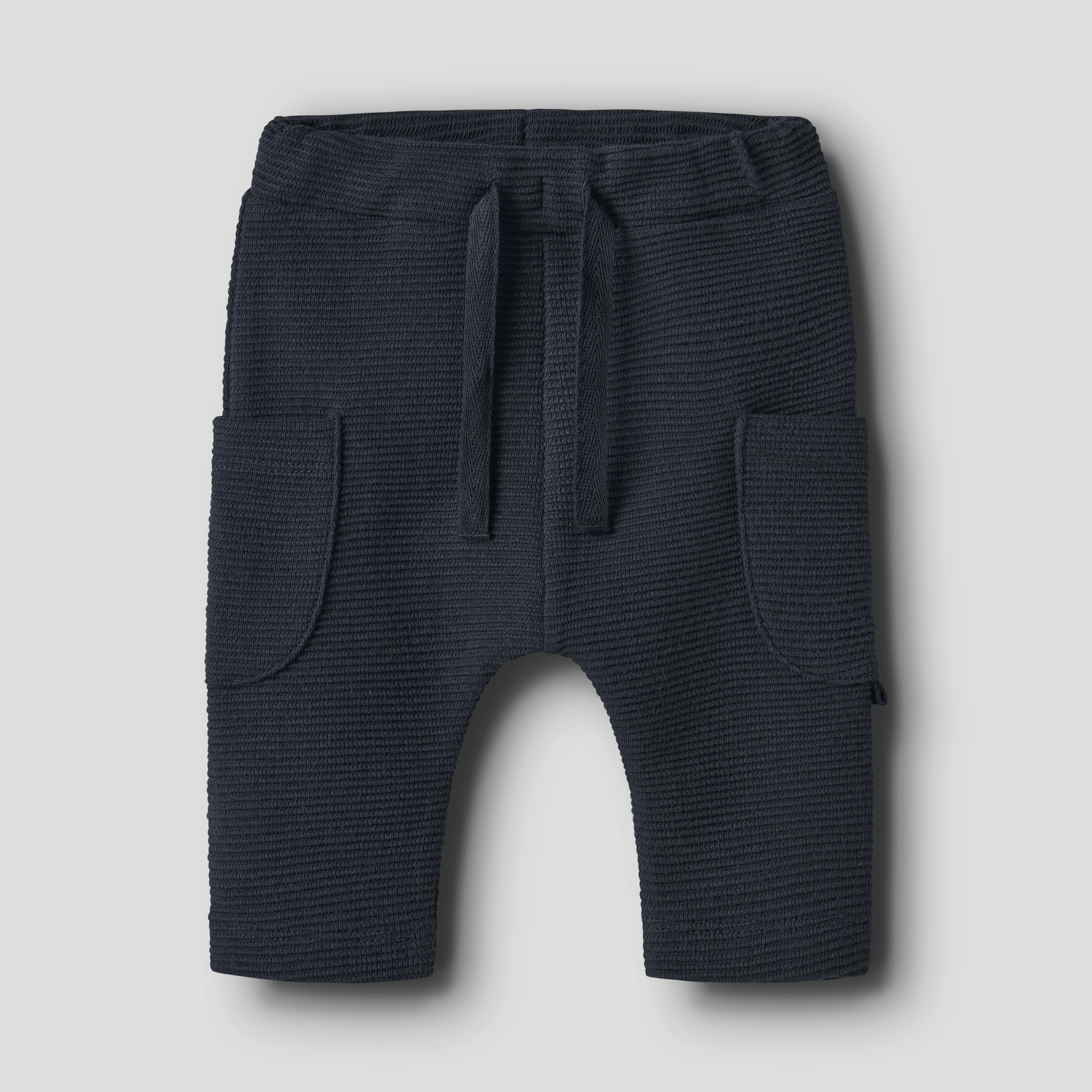 Mørkeblå strikkede baby cargobukser med snøring i midjen og to påsydde lommer, forfra.