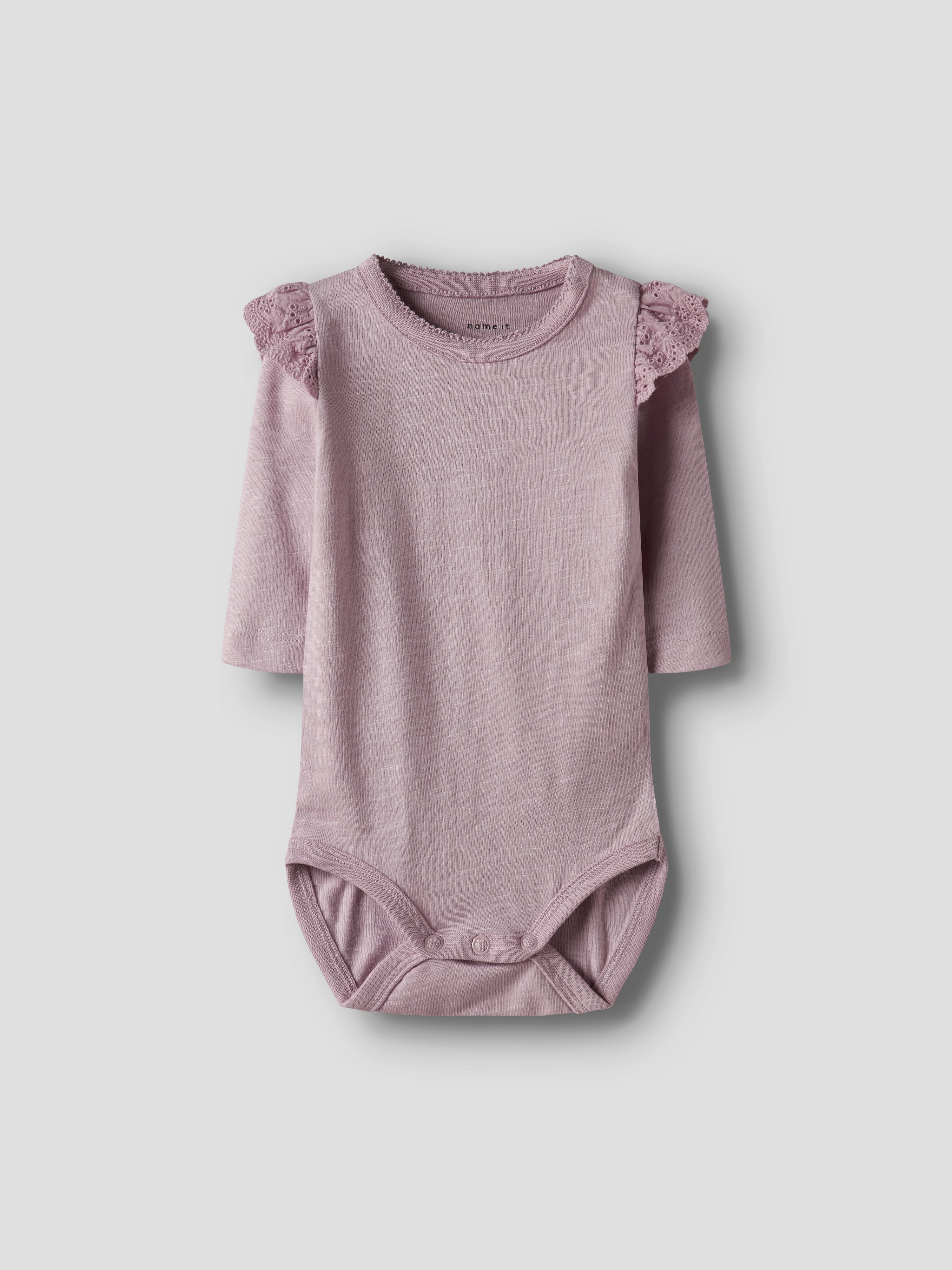 En baby lys lilla langermet body med blondevolanger på skuldrene og trykknapper, forfra.