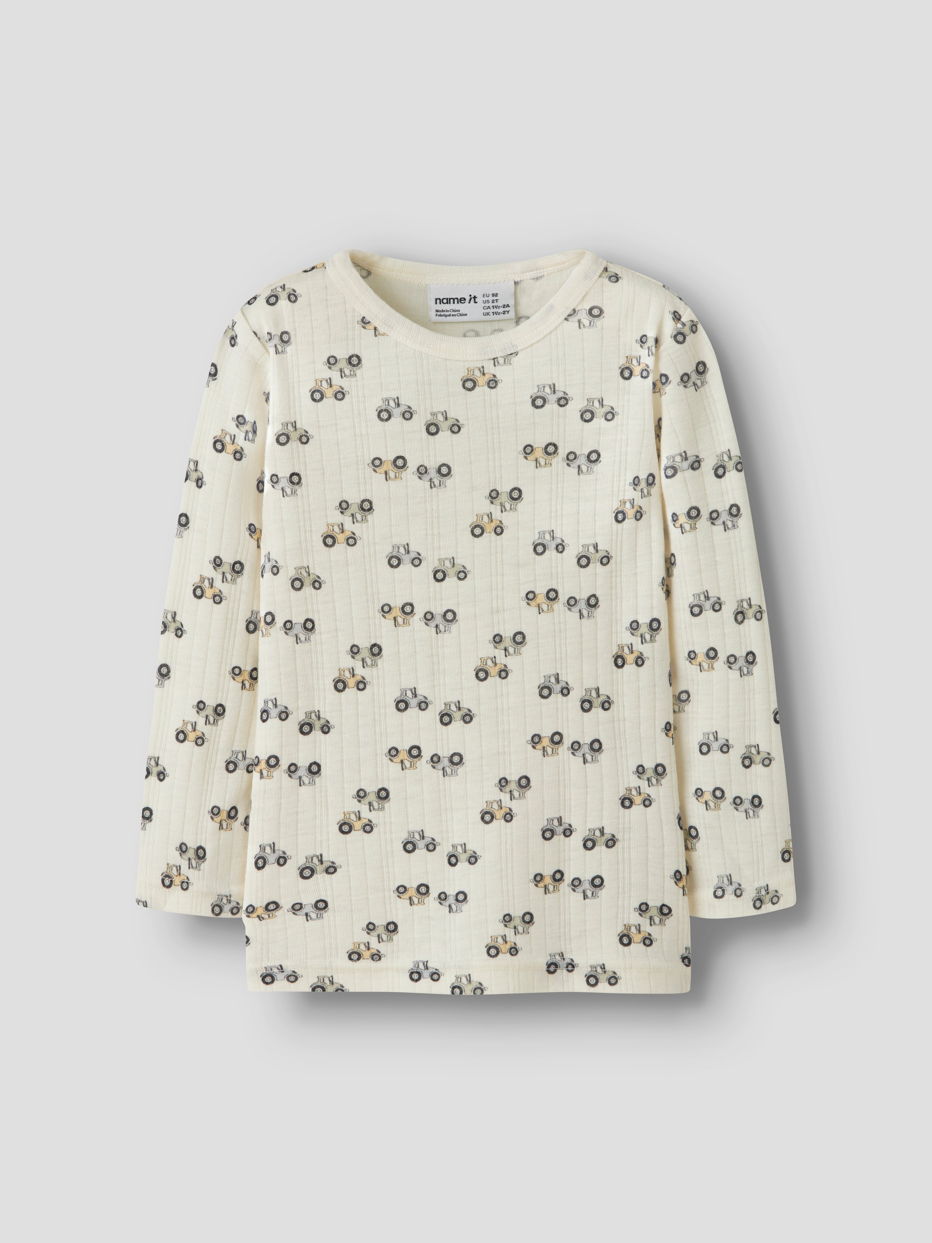 Barns kremfargede ribbet langermet topp med gjentatt mønster av gule traktorer, forfra.