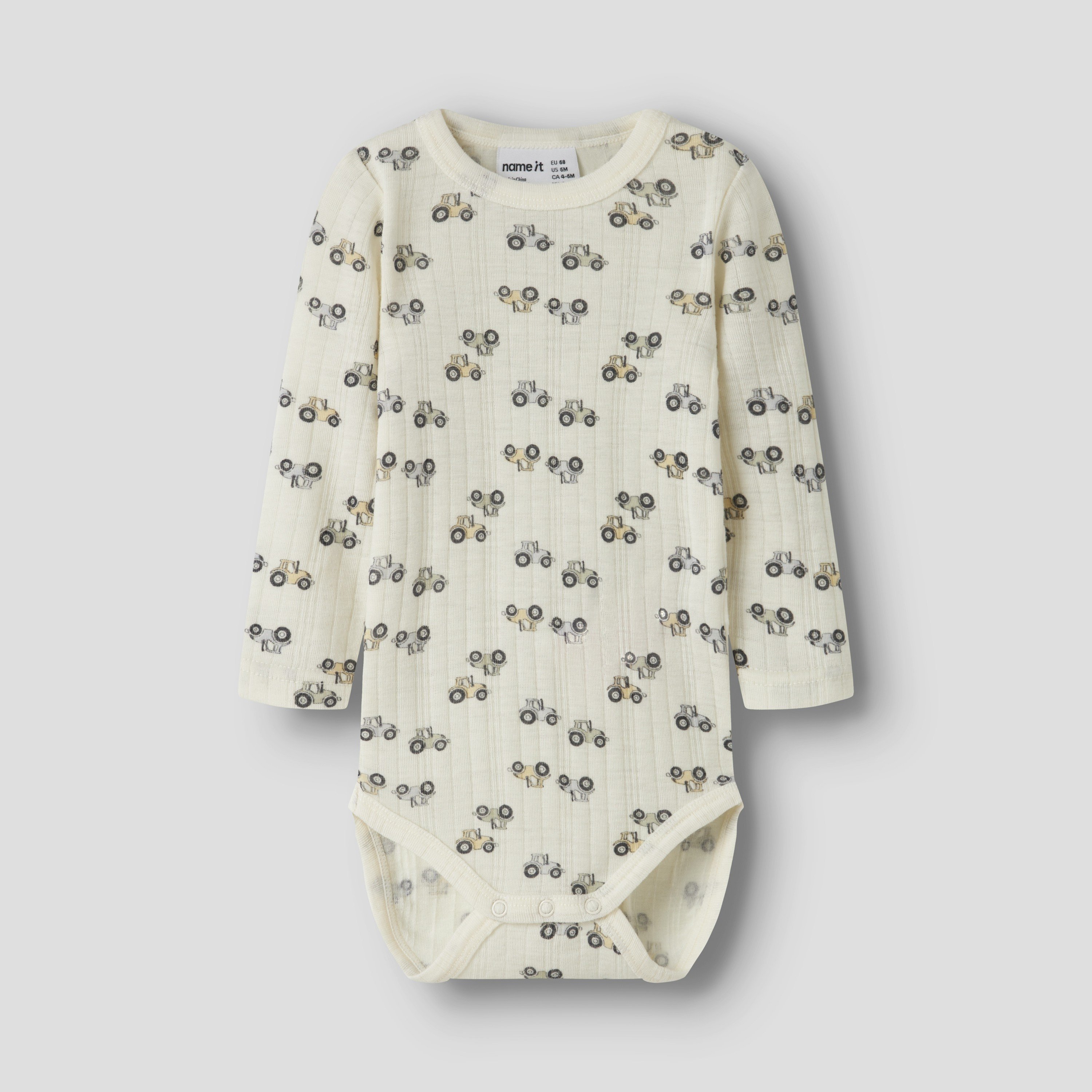 Off-white ribbet langermet babybody med heltrukket traktormønster og trykknappfeste, forfra.