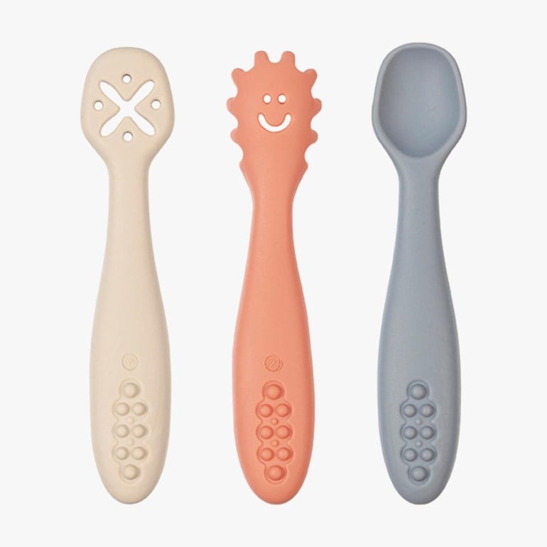 Sett med tre silikon baby skjeer/bitringer: beige X-utskåret, korall smilende sol og blå skje.