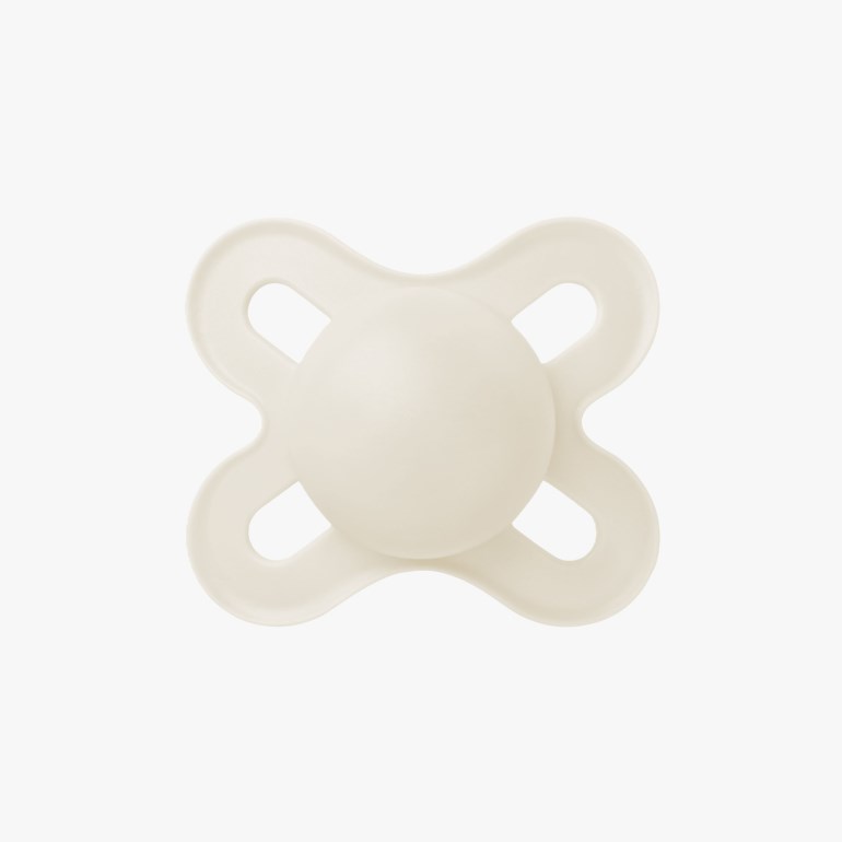 En kremfarget babynapp med sommerfuglformet skjold og en rund sentral knapp, forfra.