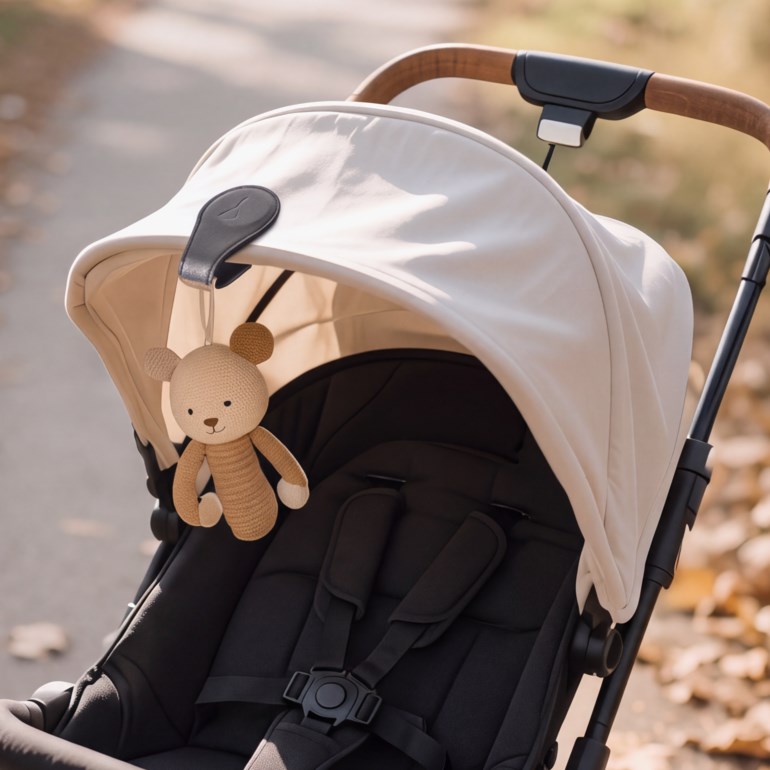 Smilende baby i kremfarget langermet genser og teppe, i svart og beige barnevogn med bamse.