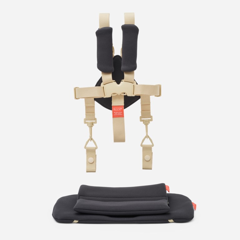 En beige babysele med svarte skulderputer og en matchende svart sittepute.