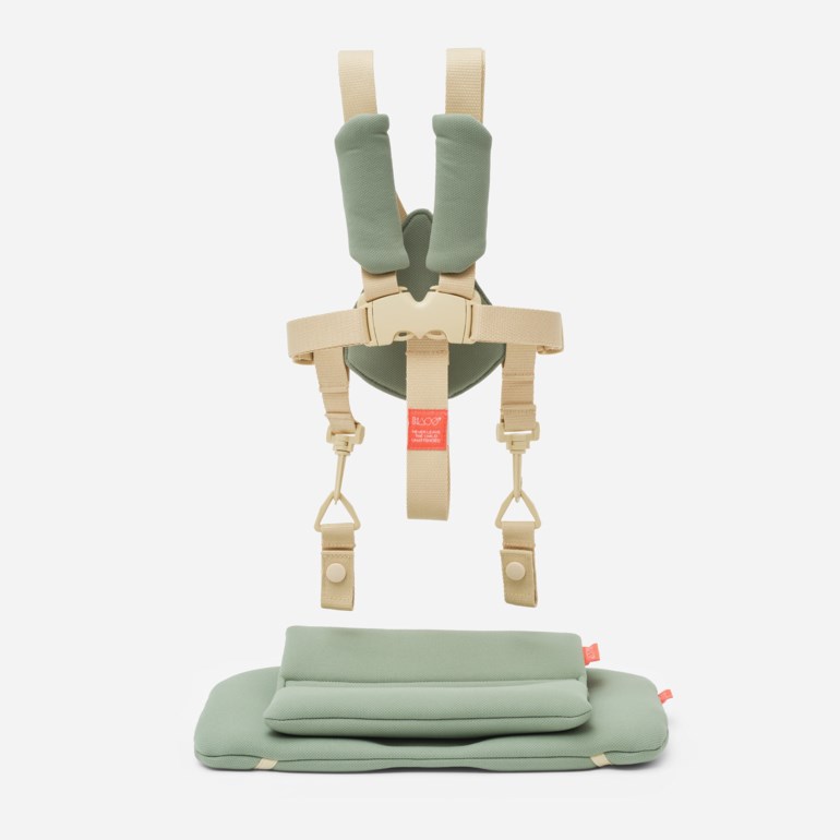 En grønn og beige babysengsele med skulderputer og spenne, ved siden av en foldet grønn babypute.