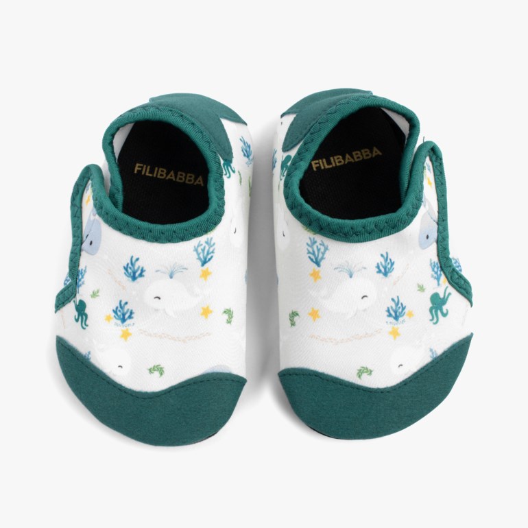 Et par hvite babysko med grønn kant og et undervannsmønster med hvaler, blekkspruter og koraller.
