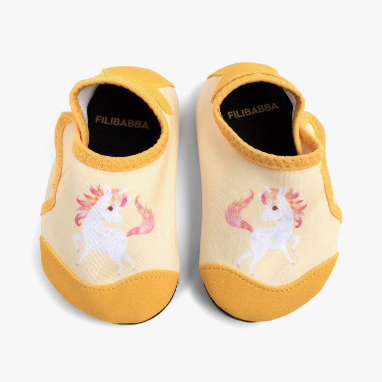 Et par gule babysvømmesko med hvitt enhjørningstrykk med rosa man og hale.