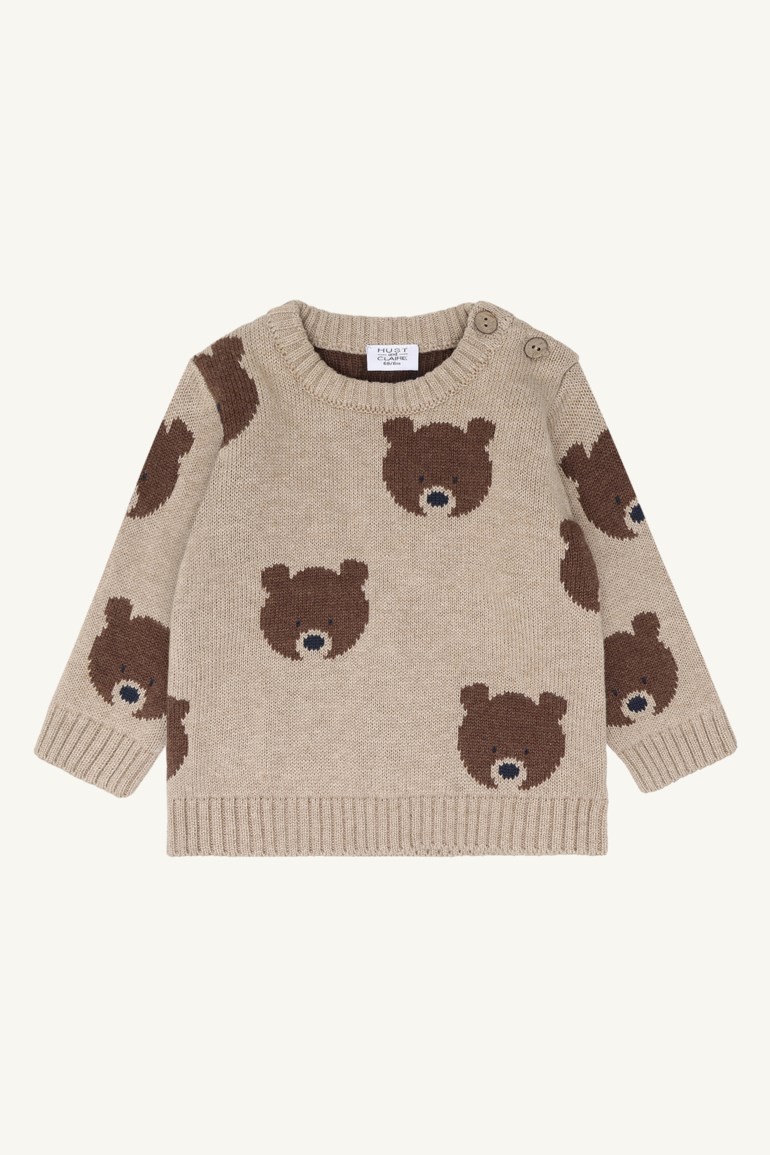 Forfra, strikket beige babysweater med mørkebrune bjørnemotiver og to knapper på skulderen.