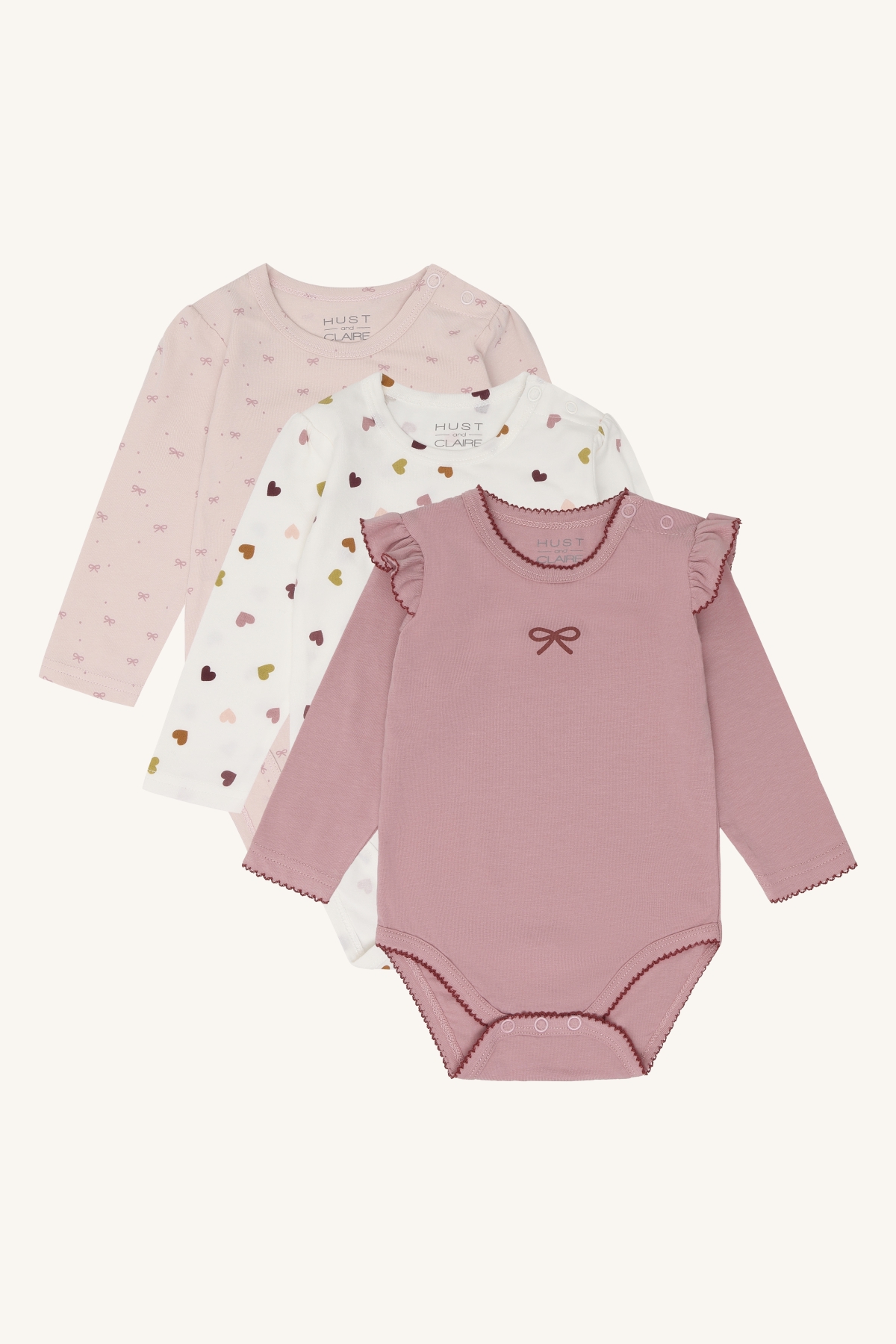 Støvrosa babybody med rysjer på ermene og sløyfe, samt to babybodyer med hjerte- og sløyfemønster.