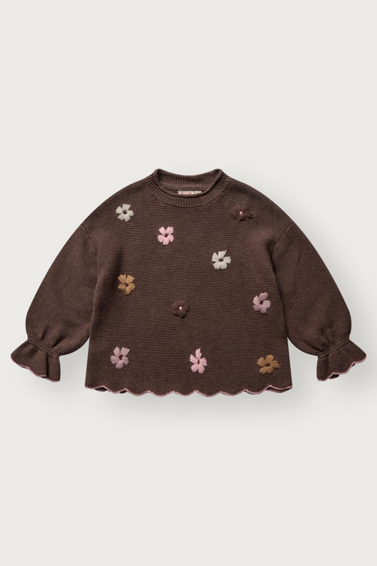 Brun strikket barnsgenser med fargerike blomsterapplikasjoner, ribbet tekstur, volangermer og rosa bølget nederkant.