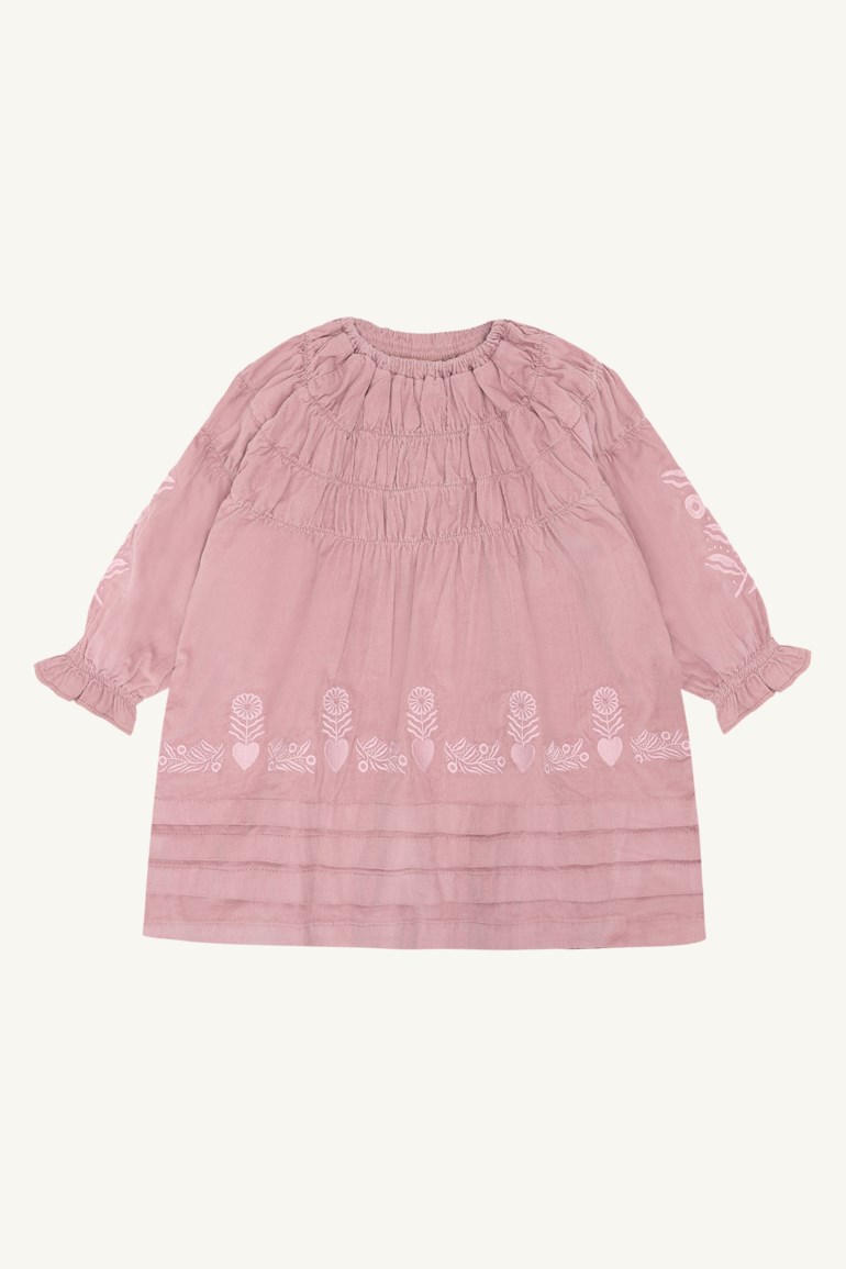 Frontbilde av en rosa langermet kjole med rynket hals, blomster- og hjertebroderi og volangmansjetter.