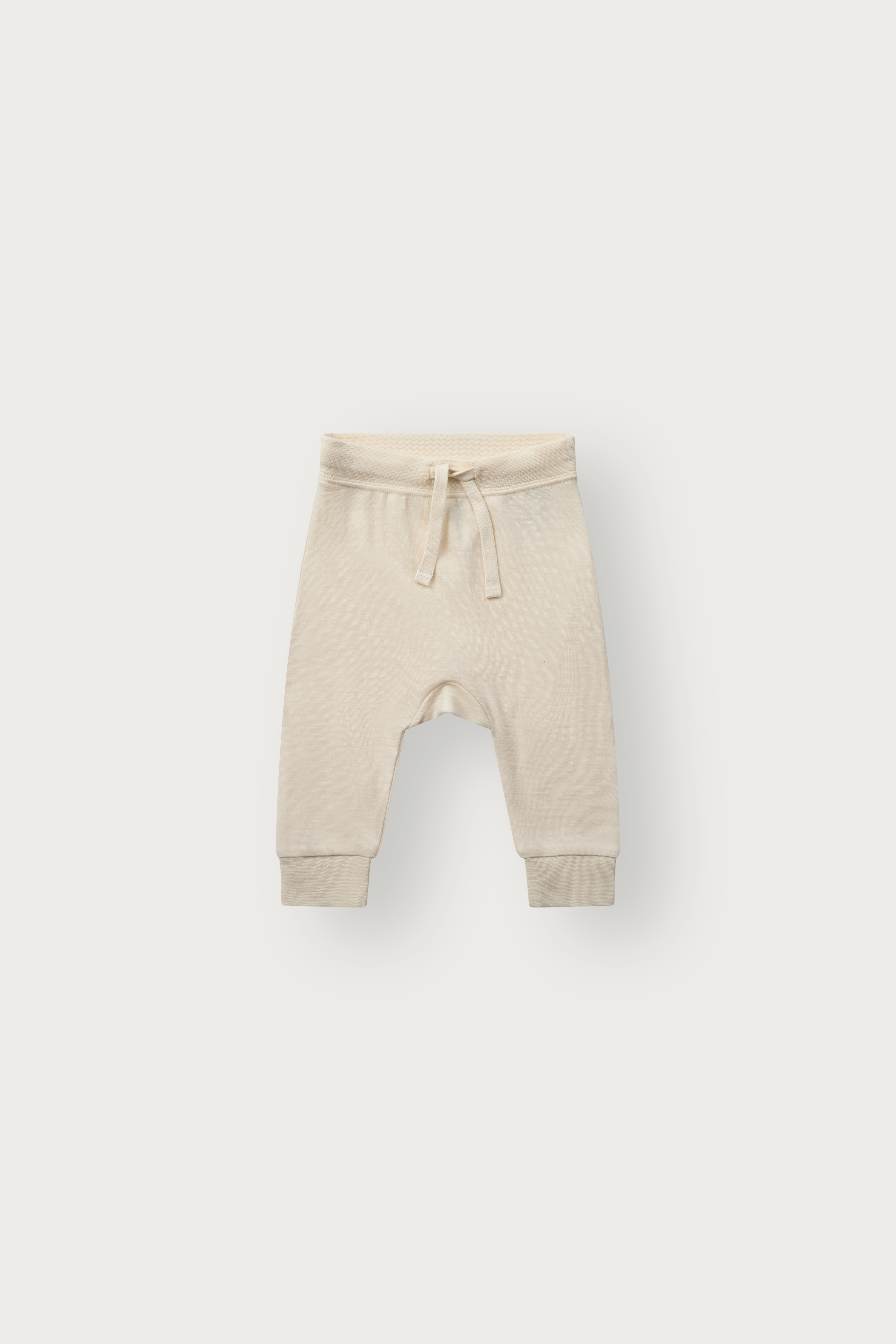 Forfra lysebeige babybukse med elastisk snøring i midjen og mansjetter ved anklene.