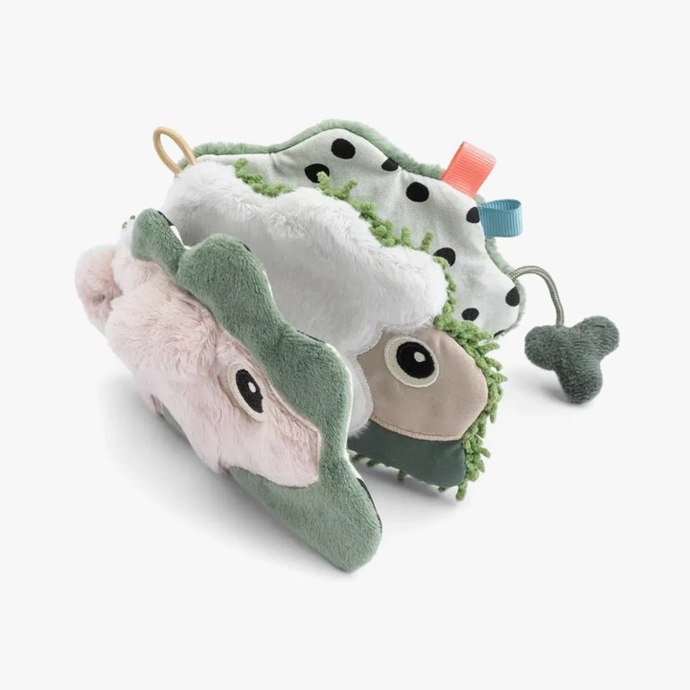 Myk baby aktivitetsbok med grønn, rosa, hvit plysj dinosaur, prikker, teksturer og en dinglende sjarm.