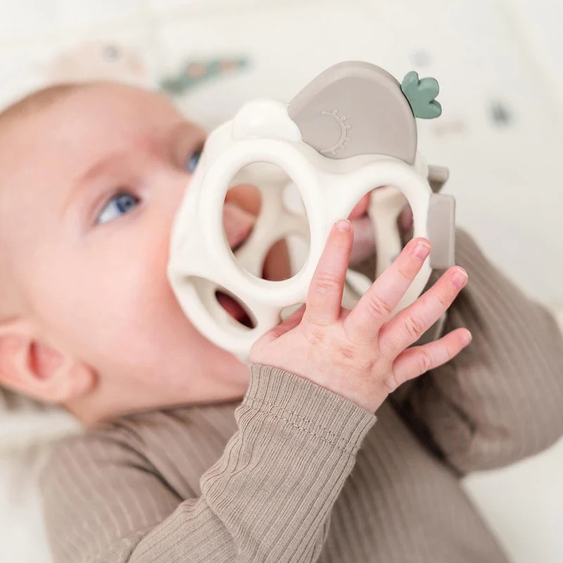Hvit geometrisk bitering med grå topp, holdt av baby i lysbrun ribbestrikket langermet topp.