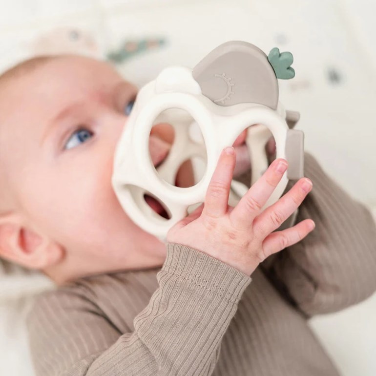Hvit geometrisk bitering med grå topp, holdt av baby i lysbrun ribbestrikket langermet topp.