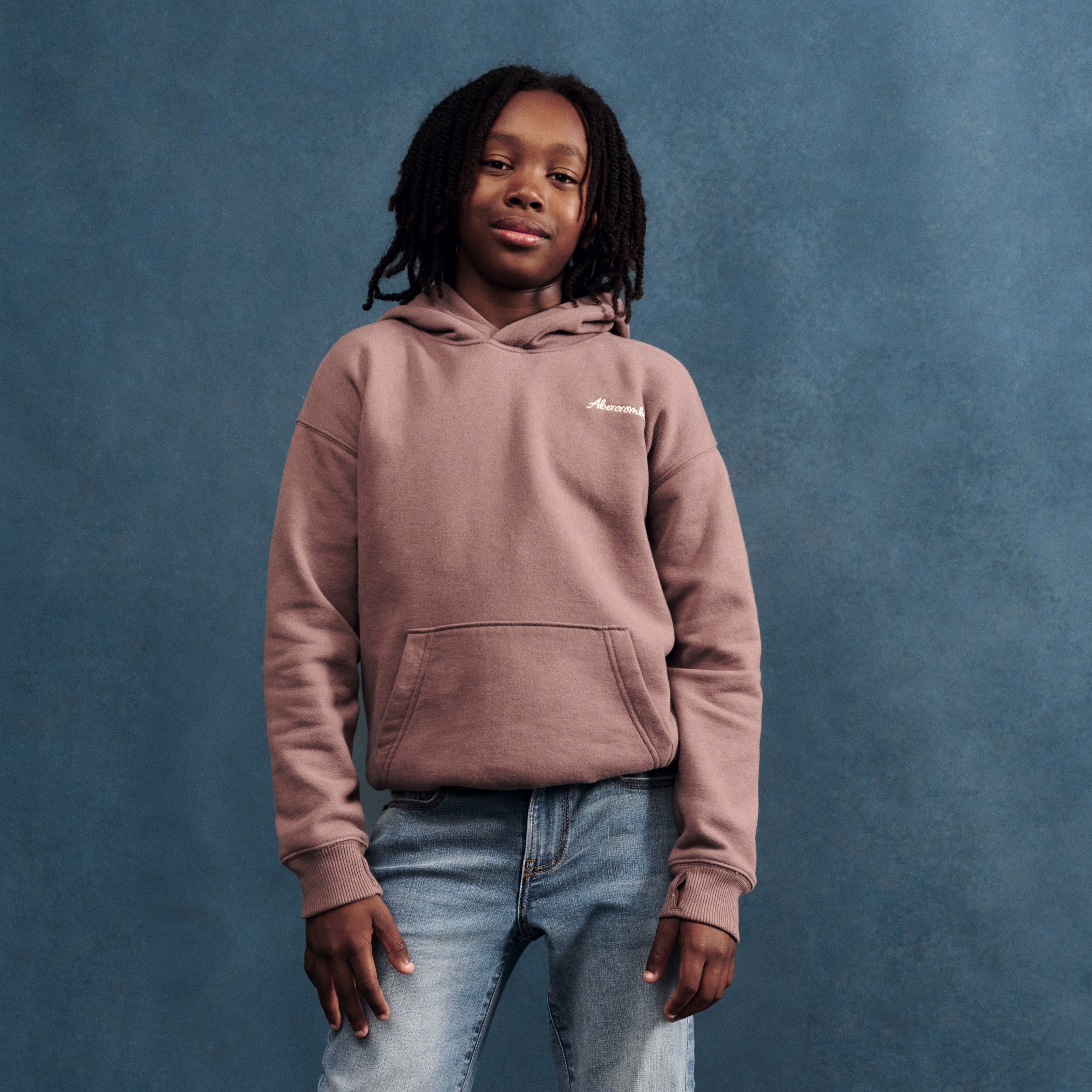 Barn bærer en støvete rosa hettegenser med 'Awesome' broderi, frontlomme og lyseblå jeans.