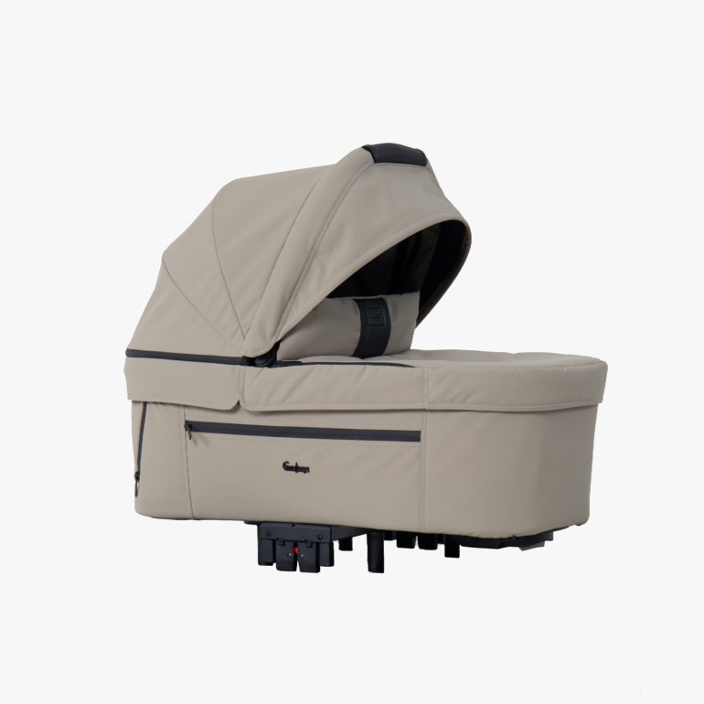En beige liggedel/barnevognskurv med kalesje, svarte detaljer og festepunkter, sett fra siden.