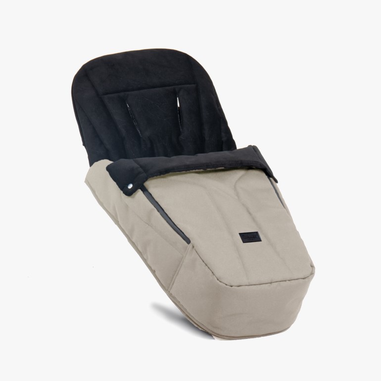 Beige babyvognpose med svart polstret for, glidelås på siden og trykknapper, vinklet forfra.