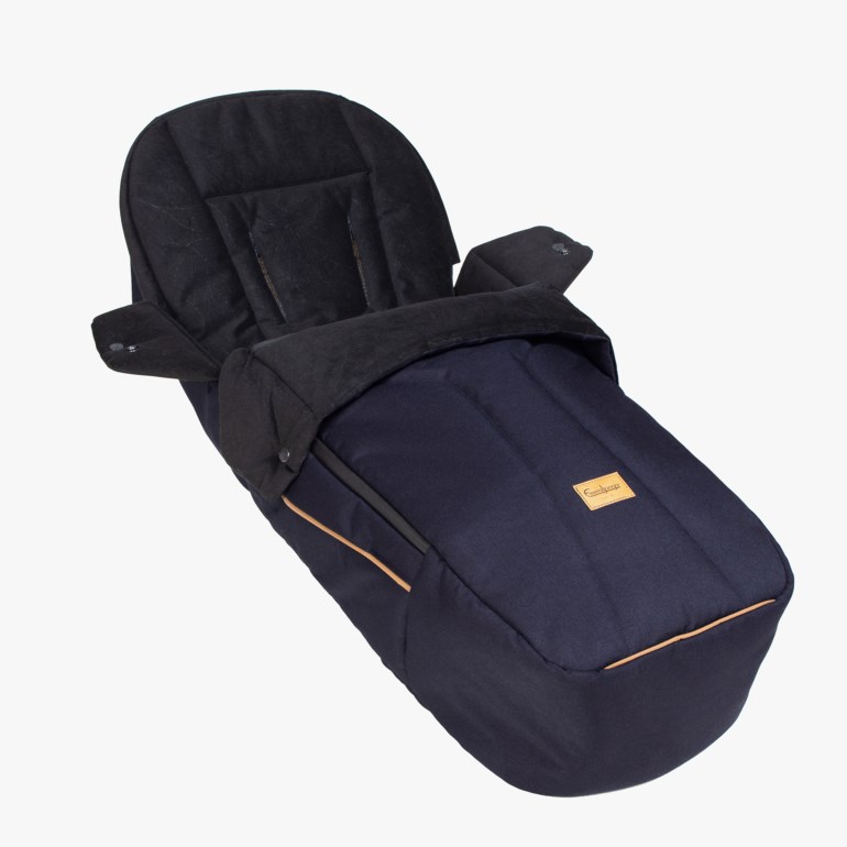 Mørkeblå polstret babyfotpose med svart topp, brun kant og glidelås, forfra.