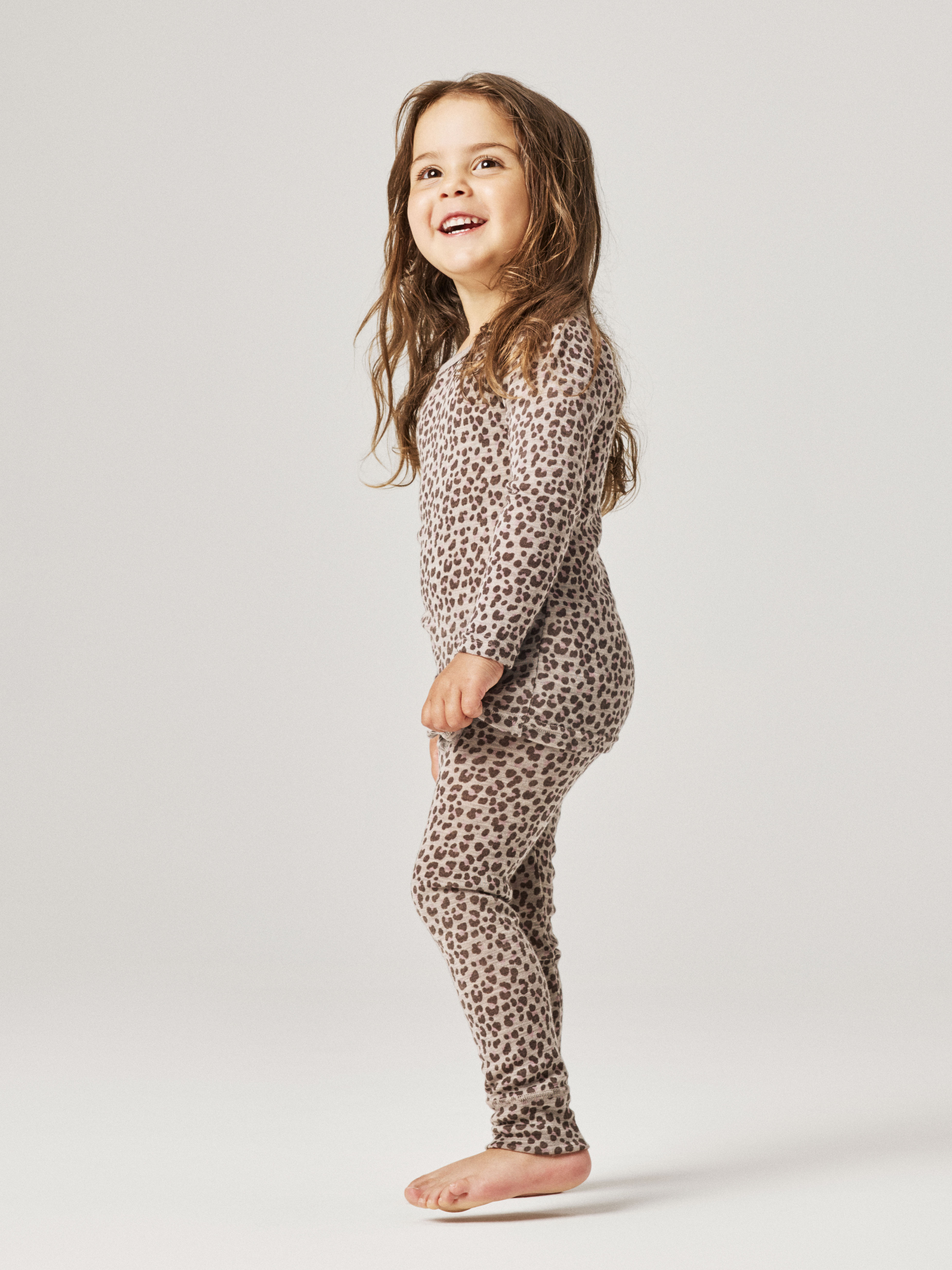 Barn har på seg et todelt beige pyjamas-sett med leopardmønster, lange ermer og lange leggings.