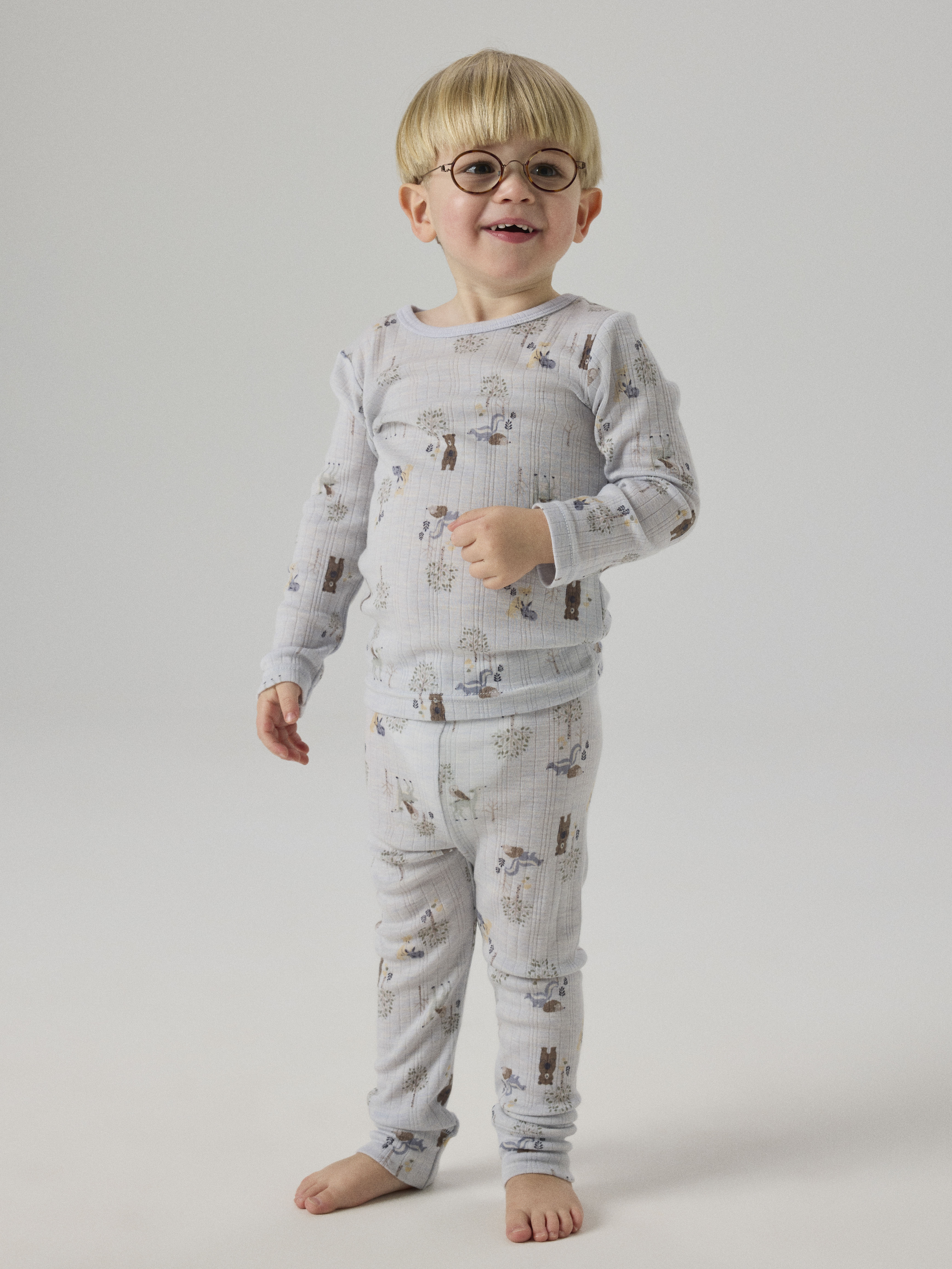 Et barn har på seg et lyseblått ribbestrikket todelt pyjamasett med skogsdyrmønster, sett forfra.