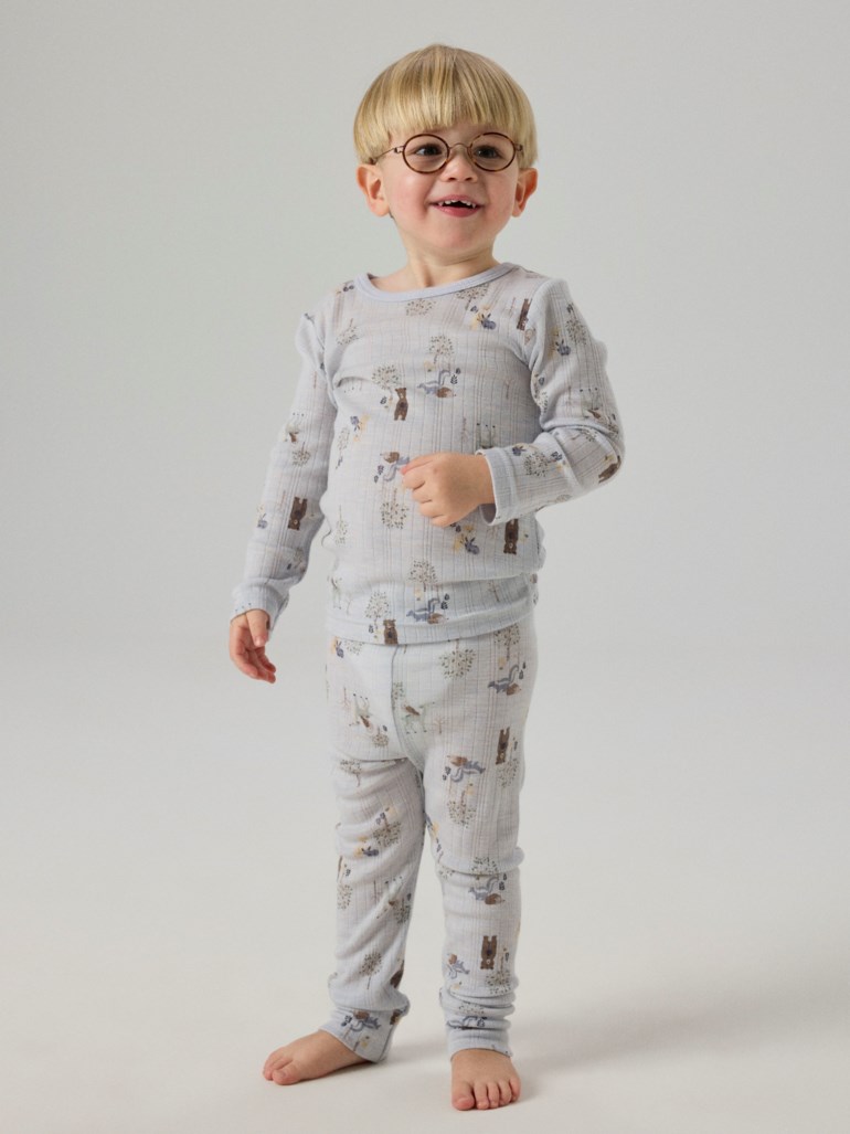 Et barn har på seg et lyseblått ribbestrikket todelt pyjamasett med skogsdyrmønster, sett forfra.