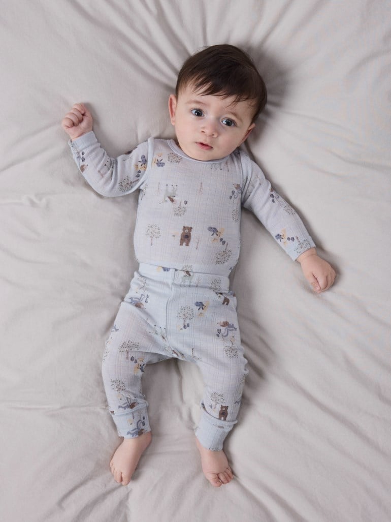 Baby har på seg et lyseblått ribbet sett med et heldekkende dyre- og tretrykk.