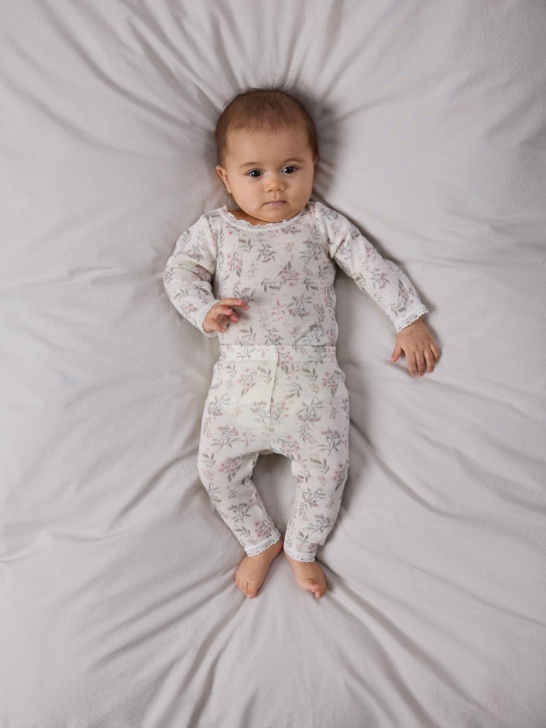 Baby har på seg et todelt langermet lyst blomstret pysjamassett med blondekant.