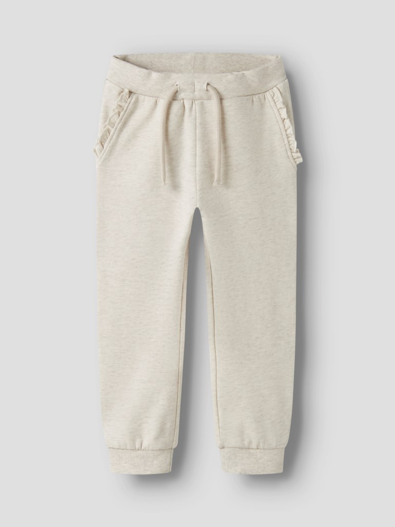 Lys beige barne-joggebukse med snøring i midjen, volangprydde sidelommer og ribbestrikkede mansjetter, forfra.