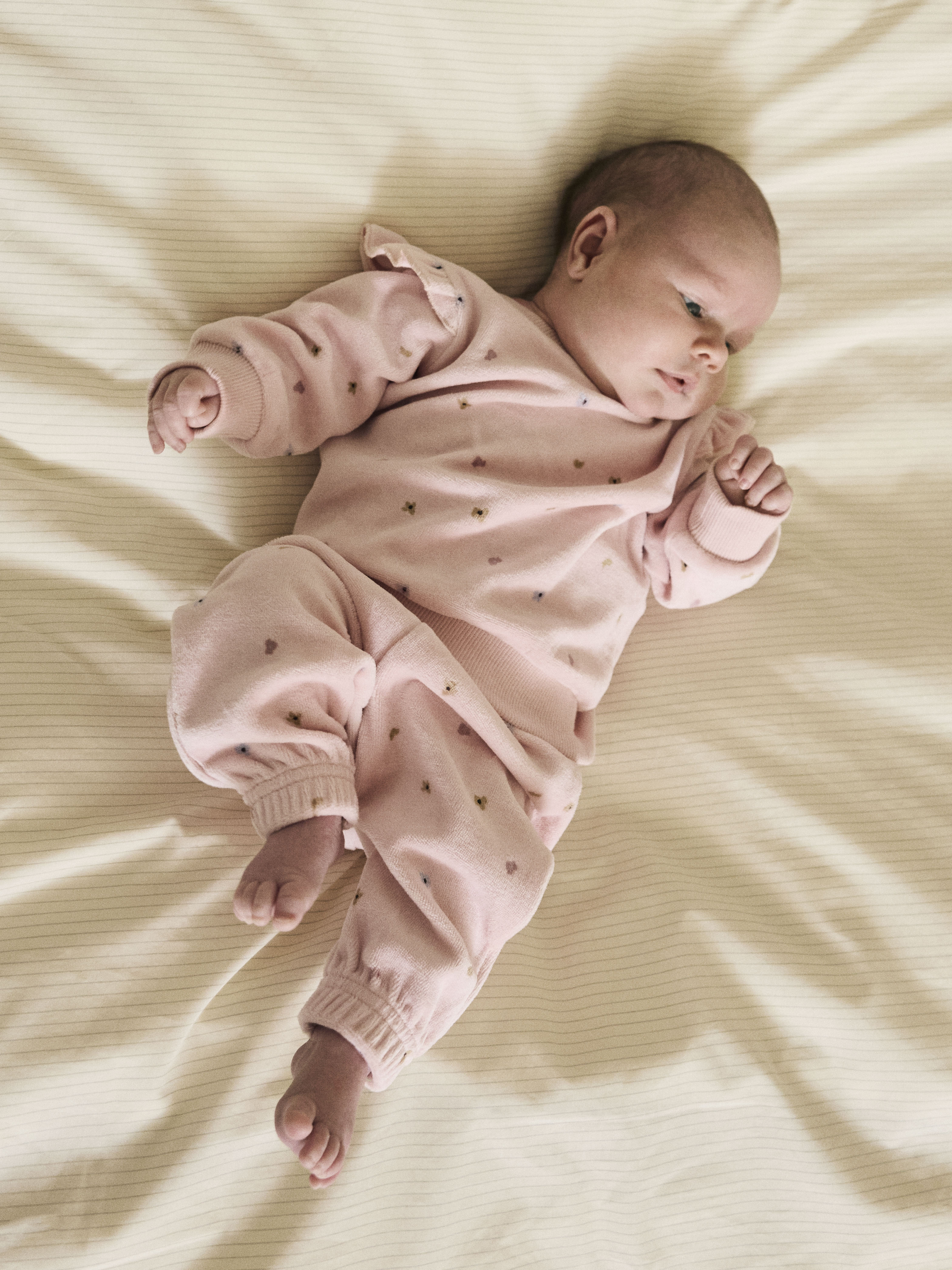 En baby har på seg et rosa todelt myksett med volangskuldre og små hjertemønstre.