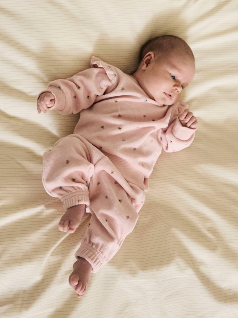 En baby har på seg et rosa todelt myksett med volangskuldre og små hjertemønstre.