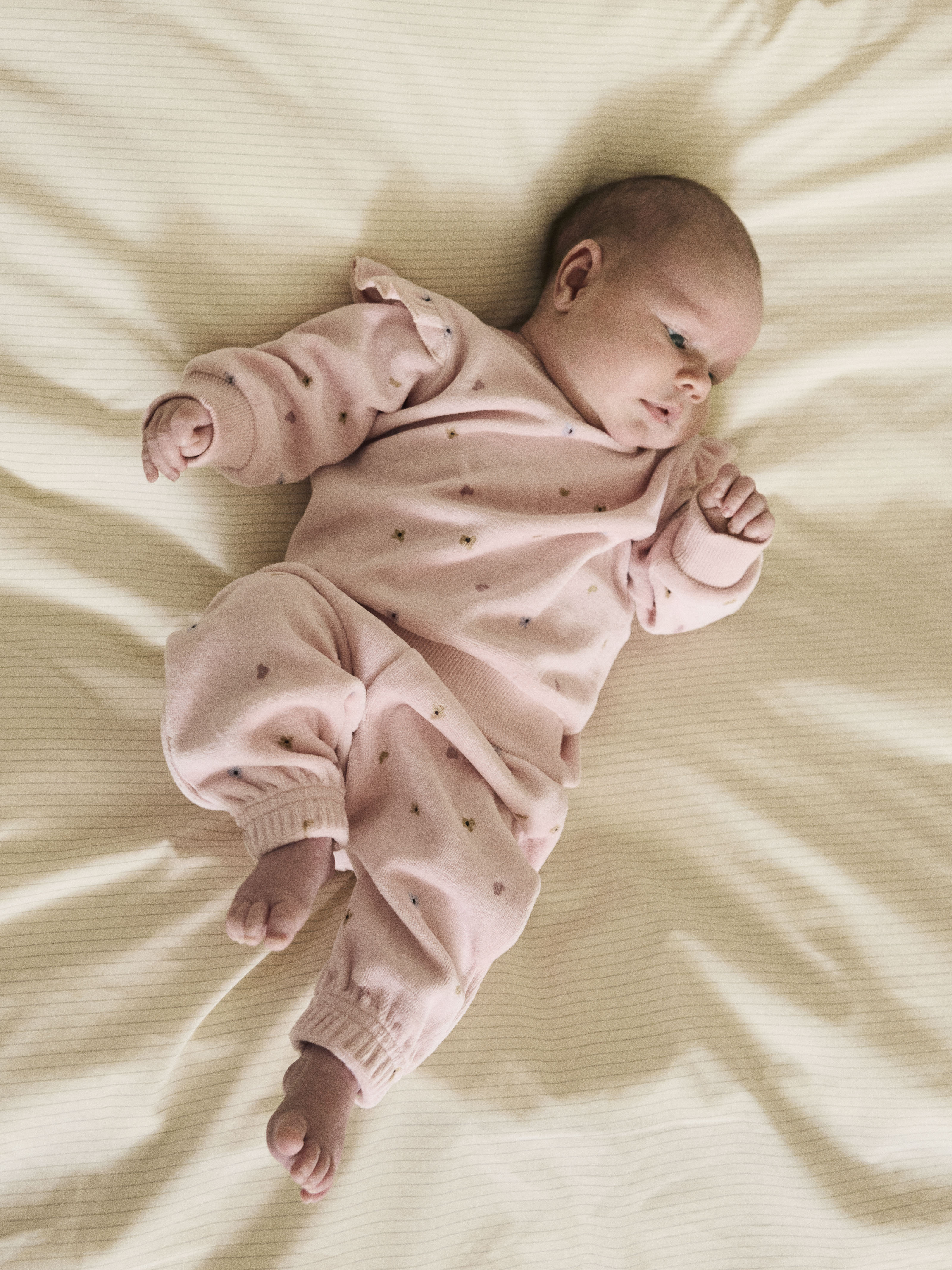 Baby har på seg et rosa todelt sett med genser og bukser med små blomstermønster.