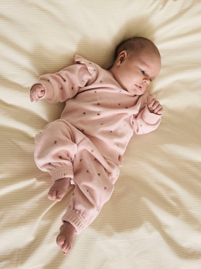 Baby har på seg et rosa todelt sett med genser og bukser med små blomstermønster.