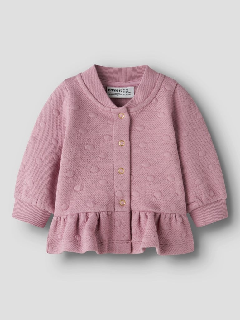Forfra, en rosa babycardigan med prikket mønster, gullfargede knapper og volang nederst.