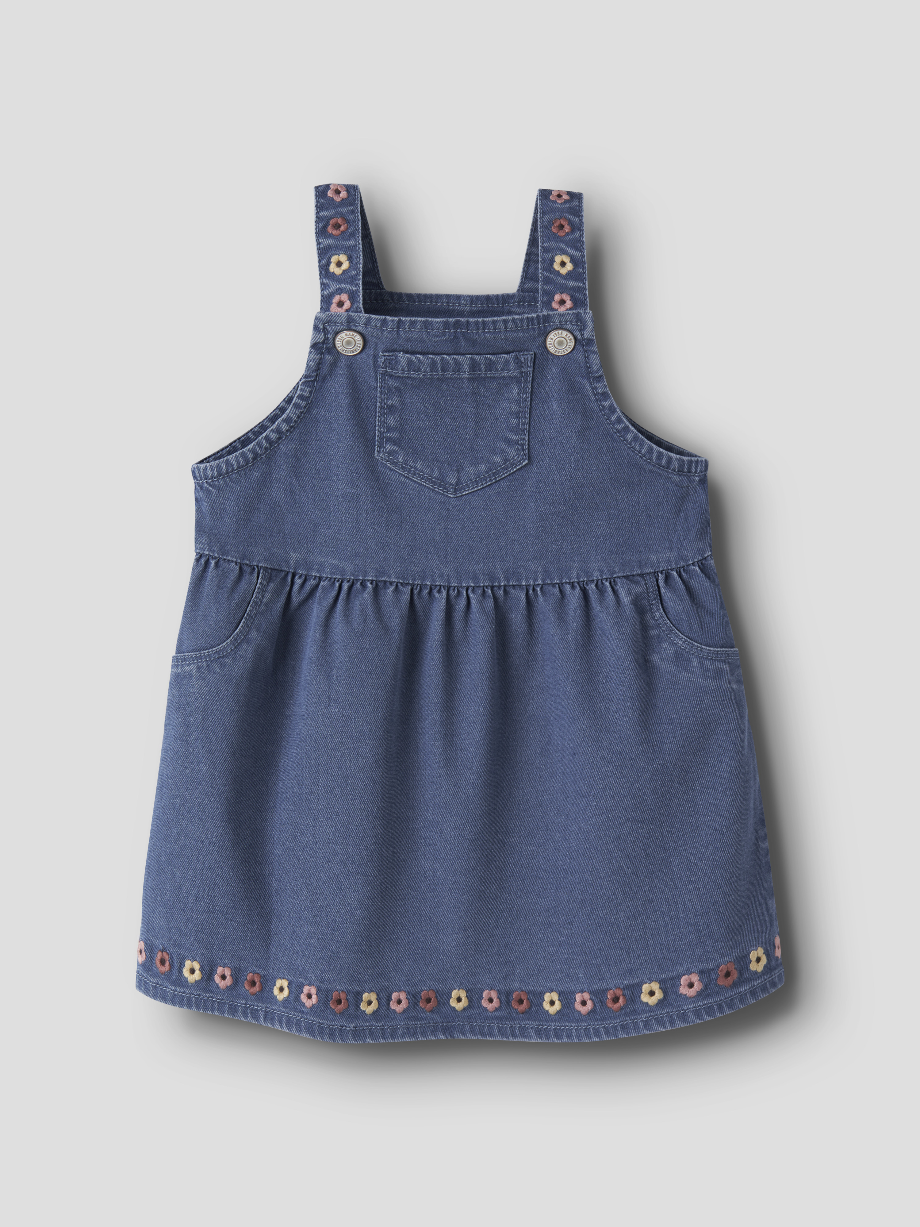 Barnas blå denimkjole med seler og broderte blomster på seler og nederkant, forfra.